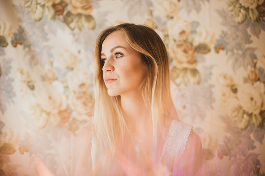 Portrait of pretty young blonde in vintage white dress and floral background backdrop
