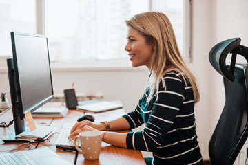 Cheerful woman sitting in an office at a desk with a computer.