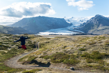 Fototapeta na wymiar Silueta de un hombre saltando en el valle de Kvíármýrarkamkur la lengua glaciar Kviarjokull al fondo. Islandia