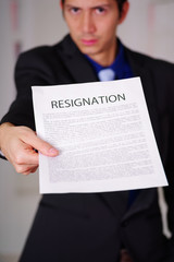 Close up of boss wearing a suit and giving a sheet of paper of resignation of contract text on it, in a blurred background