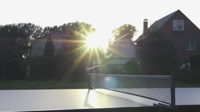A small white ball for table tennis flies at the net against a beautiful sunset with rays of the sun. slowmotion, 1920x1080, hd