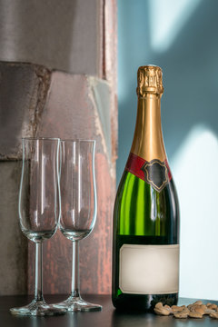 Still life shot of a unopened champagne bottle and two empty glasses on a table with snacks. Label with copy space.