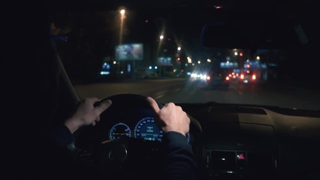 Hands on the wheel. The driver driving a black car at night.