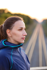 Portrait of young sporty woman on bridge in the evening. Athletic girl standing outdoor after fitness training
