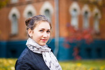 Fototapeta premium Young female student standing near college building in autumn. Education background with student girl and copy space