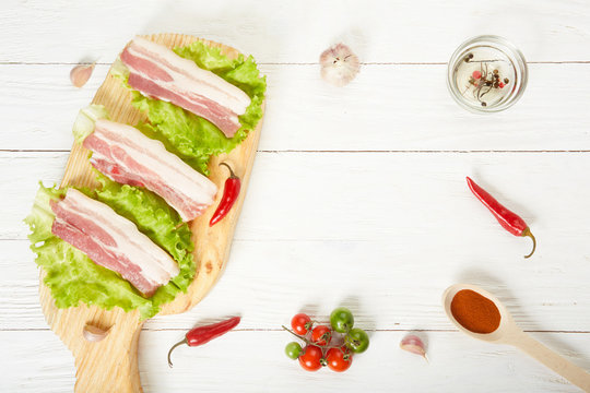 Raw Pork Meat Brisket Bacon On Chopping Board With Lettuce Cherry Tomatoes Spices From Above