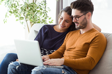 Beautiful young couple using laptop on the sofa at home.