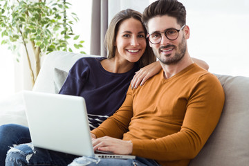 Beautiful young couple using laptop on the sofa at home.
