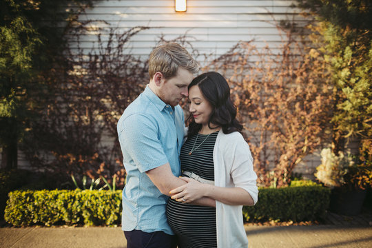 Young expecting couple holding each other outside