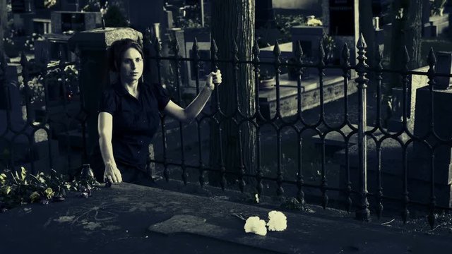 Young woman sitting on cemetery tomb and having horrified expression. He responds to a haunted revelation. Color-styled horror and scary scene.
