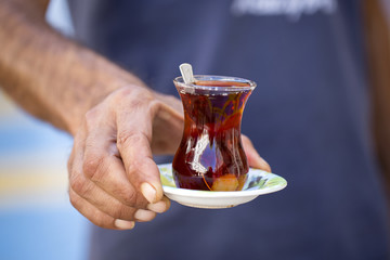 Delicious red Turkish tea with traditional pear shaped glass with a teaspoon in the man hand
