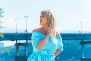 A middle-aged woman, plus in a light blue dress, rests on a city waterfront on a day off. The...