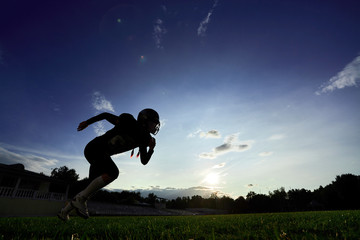 The American football player runs across the field at sunset.