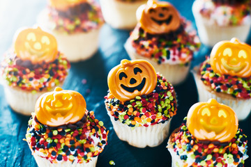 Fototapeta na wymiar festive halloween pumpkin cupcakes with chocolate frosting and colorful sprinkles
