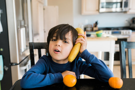 Child Holds A Banana Up To His Ear As If A Telephone