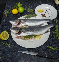 Raw fish with lemon and rosemary on a white plate.