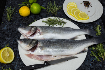Raw fish with lemon and rosemary on a white plate.