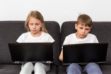 Two children with computers on the couch