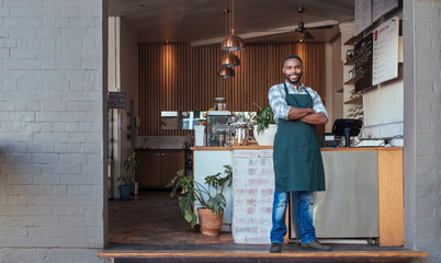 Smiling African entrepreneur standing welcomingly in front of his cafe