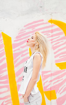 Hip beautiful female in front of yellow and pink wall with graffiti.