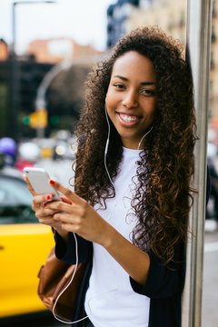 Young african american woman using her smart phone whilst waiting for the bus.