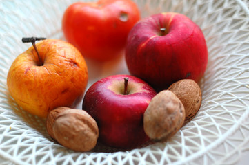 Red and orange apples and walnuts on a white plastic wicker plate. Autumn mood, harvest concept
