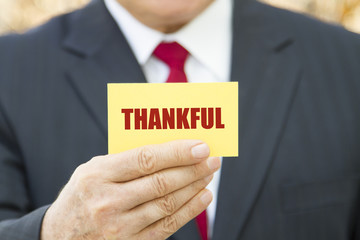 Businessman showing a card with text THANKFUL