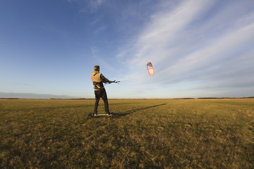 Young man kiteboarding in the field at sunset