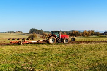Obraz premium Red tractor pole field. Autumn field work. Life on the farm. Agricultural landscape in the Czech Republic.