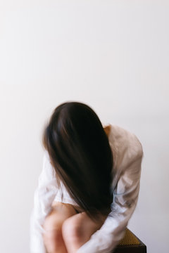 Unrecognisable woman leaning forward, hugging her knees, intentional movement and blur