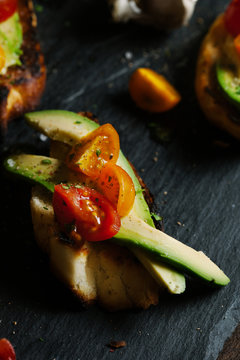 Slice of crostini with avocado and tomato.