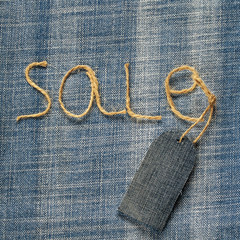 denim fabric background with the inscription sale of twine in  hand and a blank price tag