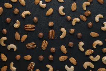 Variety of mixed nuts - almond, hazelnuts and cashew - on the dark slate background with copy space. Top view. Toned