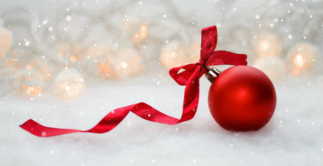 red Christmas ball with bow of red ribbon on a background of garlands and artificial snow