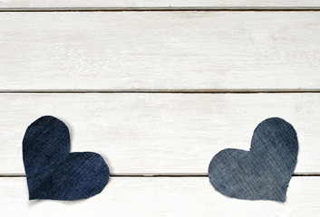  two stylish hearts are cut from blue denim fabric lying on a white wooden background
