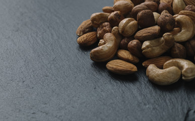 Variety of mixed nuts - almond, hazelnuts and cashew - on the dark slate background with copy space. Top view. Toned
