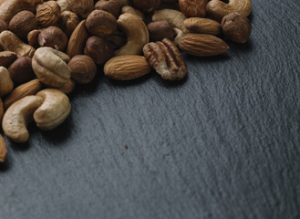 Variety of mixed nuts - almond, hazelnuts and cashew - on the dark slate background with copy space. Top view. Toned