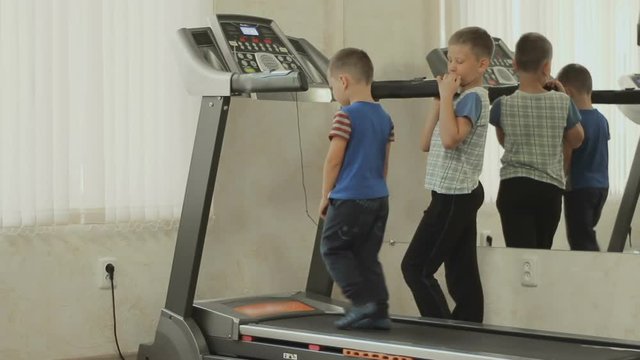 the older child is training the younger to walk on the treadmill. The kid with the trainer trains in the gym near the mirror. The concept of a healthy lifestyle. Baby cares about body and health
