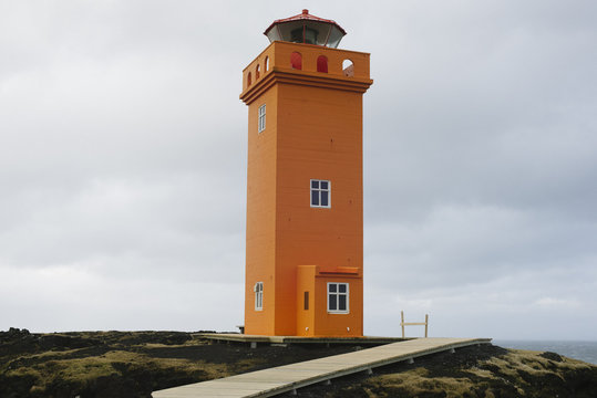 A square orange lighthouse on the top of a cliff.