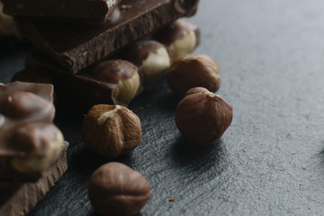 Chocolate bar pieces and nuts on dark background with copy space. Chocolate background. Toned