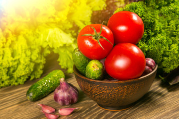 Tomatoes, garlic bulb and cucumbers on a wooden table. Green salad in the background. The concept of a healthy diet