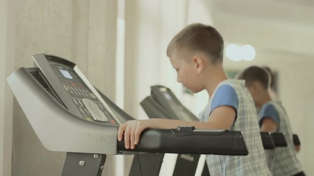 Teenager walks on the treadmill. the kid is exercising in the gym near the mirror. Boy cares about his body, figure, appearance and health from the childhood. The concept of a healthy lifestyle