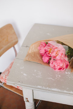 Table with bright pink peonies wrapped in brown paper