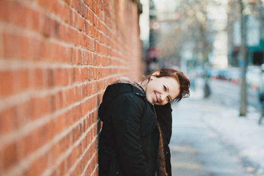 Woman smiling bashfully at camera, standing against brick wall