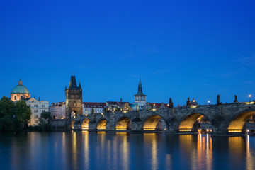 Fototapeta na wymiar Lit Charles Bridge (Karluv most) and old buildings at the Old Town and their reflections on the Vltava River in Prague, Czech Republic, at dusk. Copy space.