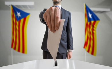 Election or referendum in Catalonia. Voter holds envelope in hand above ballot. Catalonian flags in...