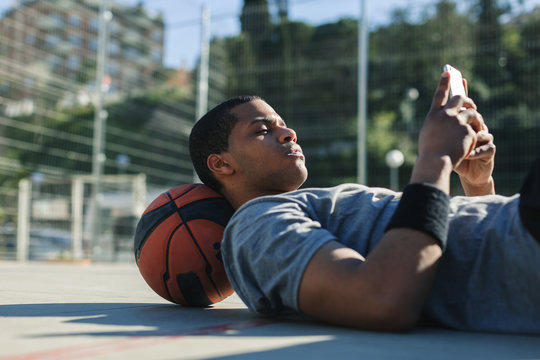 Male basketball player using his smartphone resting after training session.