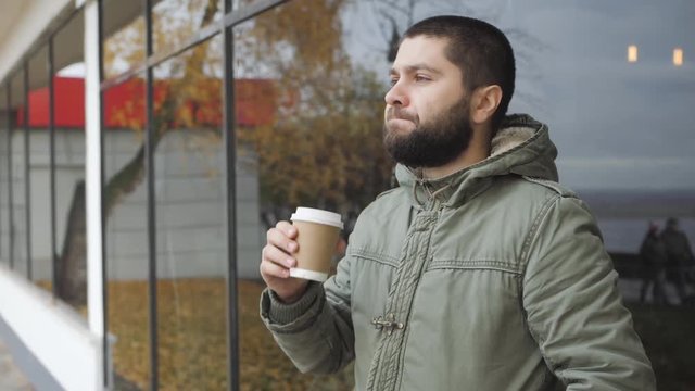 Handsome young bearded man is holding a cup. drinking hot drink coffee or tea in autumn outdoors