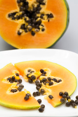 Papaya fruit - half and slice with seeds and light grey background
