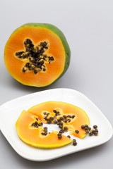 Papaya fruit - half and slice with seeds and light grey background
